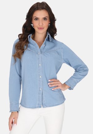 Camicia di denim azzurro chiaro con maniche lunghe, chiusura con bottoni davanti, colletto a punta e polsini arricciati. Presenta dettagli cuciti sul petto.