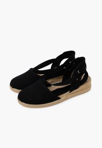 Espadrilles de lona negra con suela de yute trenzado, que cuentan con correas entrecruzadas y ojales en el talón para mayor ajuste.