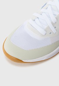 Hvite mesh sportssko med lysegrønne detaljer og en teksturert gummisåle. Har flate lisser og en rund tådesign.