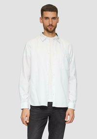 Valkoinen pitkähihaiset napillinen paita slim fit -mallilla, jossa on rintatasku, sileä pinta ja hienoinen kiilto, käytetty valkoisen t-paidan päällä.