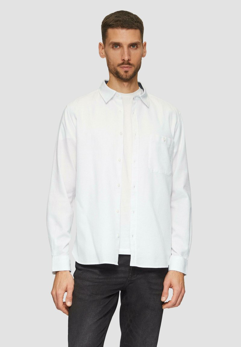 Valkoinen pitkähihaiset napillinen paita slim fit -mallilla, jossa on rintatasku, sileä pinta ja hienoinen kiilto, käytetty valkoisen t-paidan päällä.