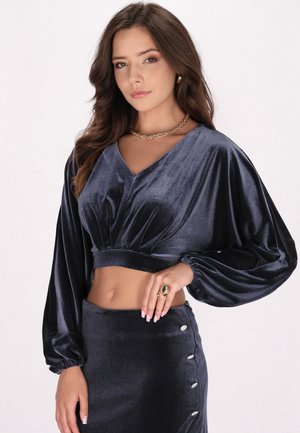 Crop top din catifea bleumarin închis, cu mâneci lungi și puffate și un decolteu în formă de V. Asortat cu o fustă lungă, cu talie înaltă, care are detalii cu nasturi.