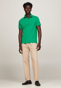 Groene polo met korte mouwen en een klassieke kraag, gecombineerd met lichtbeige chinos en zwarte schoenen, wat zorgt voor een casual outfit.