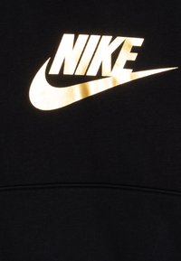 Sweatshirt preto com um logotipo da Nike em dourado metálico exibido de forma proeminente na frente. O material parece liso e com uma textura suave.