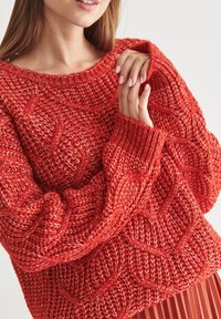 Gruby czerwony sweter z dzianiny z wzorem warkoczowym, ze ściągaczem na dekolcie i mankietach, charakteryzujący się miękką teksturą i luźnym krojem.