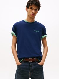 Tumši zilā t-kreklā ar īsām piedurknēm, ar zaļu apkakli. Uz krūtīm ir neliels zaļš "tommy jeans" logo. Valkāts kopā ar tumšām džinsu biksēm.