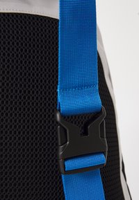 Material de malha preta com uma correia em rede azul e fecho em plástico preto. O design apresenta uma superfície texturizada para maior aderência e durabilidade.