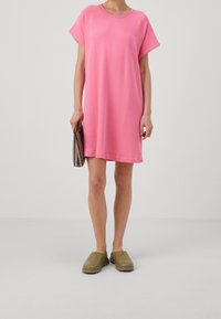Vestido corto de manga corta en color rosa, hecho de una tela suave, con un corte relajado, escote redondo y un diseño liso, acompañado de zapatos olive de tipo slip-on.