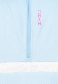 Jasnoniebieska tkanina z siateczkową teksturą, z centralnym zamkiem błyskawicznym i białym poziomym paskiem. Różowe logo w górnym lewym rogu.