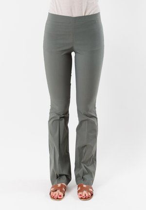 Pantaloni elastici di un verde scuro, con vita aderente, fondo svasato e superficie liscia. Indossati con sandali marroni, dotati di una suola piatta.