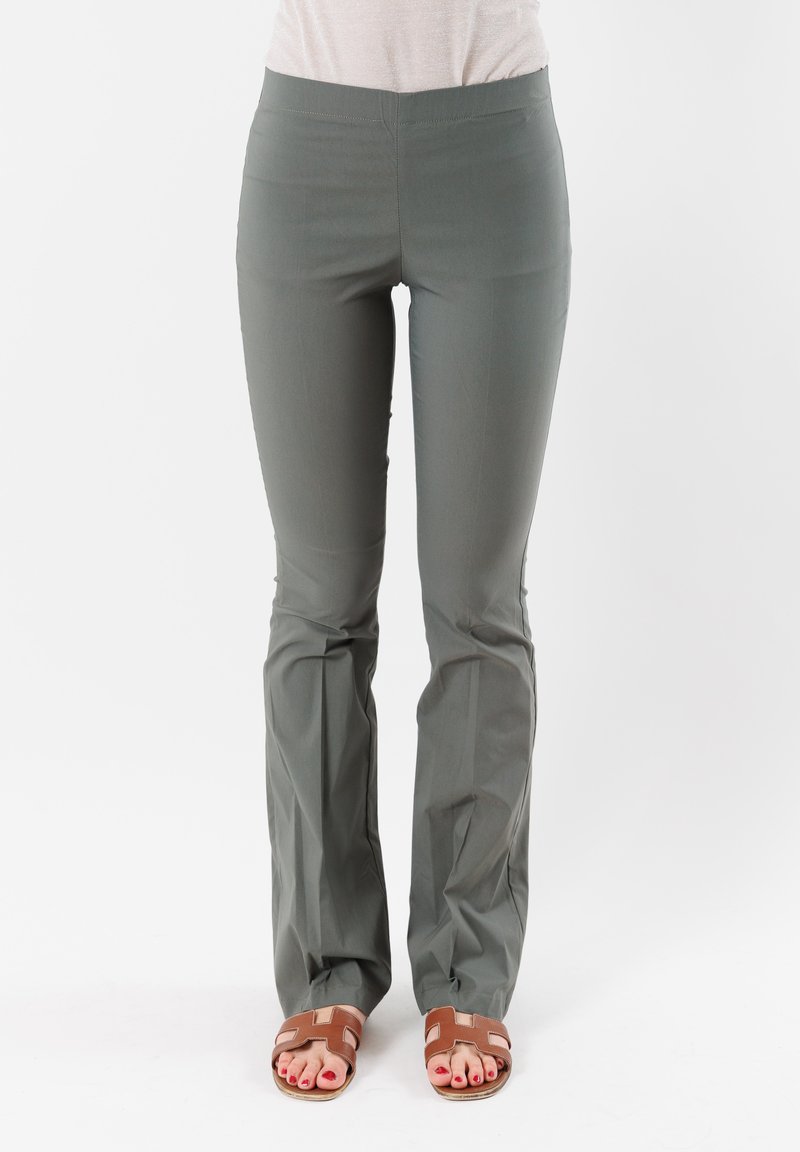 Pantaloni elastici di un verde scuro, con vita aderente, fondo svasato e superficie liscia. Indossati con sandali marroni, dotati di una suola piatta.