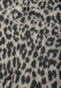 Neulekangas, jossa on vaalea beige tausta ja mustia sekä harmaita leopardi-ihopainokuvioita, esittelee pehmeän ja karhean tekstuurin.