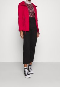 Veste légère rouge avec capuche, top noir à motifs floraux, pantalon large noir taille haute et baskets montantes noires.