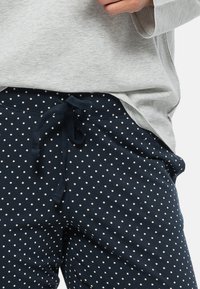 Lichtgrijze lange mouwen top gecombineerd met marineblauwe joggers met stippen, voorzien van een verstelbare trekkoord taille en een zachte, textuurachtige stof.