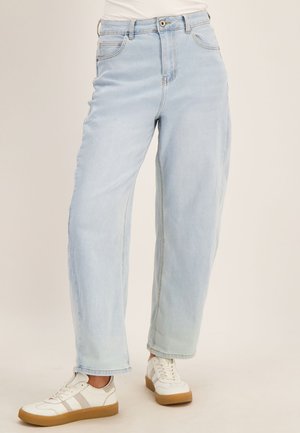 Lichtblauwe jeans met hoge taille en rechte pijpen, gedragen met witte sneakers met beige strepen en rubberen zolen.