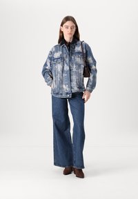 Jeansjakke med et lyseblått tie-dye mønster, kombinert med mørkeblå vide bukser og brune hælstøvler, båret med en liten veske.