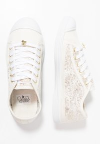 Baskets blanches avec des accents dorés, tige en textile avec un motif texturé, bout en caoutchouc blanc, et six œillets avec des lacets blancs.