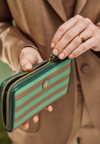 Grünes und braunes gestreiftes Portemonnaie aus strukturiertem Material. Verfügt über einen goldenen Reißverschluss, kreisförmiges Hardware-Detail und einen Reißverschlussverschluss.