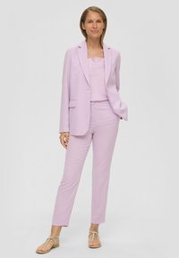 Light lavender suit featuring a fitted blazer and tailored pants. The fabric appears smooth with a subtle texture. Paired with simple sandals.