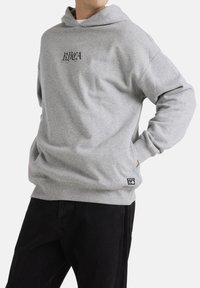 Grijze hoodie met een voorzijde kenguruzak, ribgebreide manchetten en zoom. Heeft zwarte geborduurde tekst op de borst en een merketiket in de zoom.