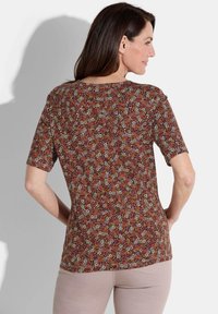 Korte mouwen top met een bloemenprint in rood, wit en gele patronen op een donkere achtergrond. Soepele stof met een relaxed fit.