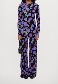 Kombinezon w kwiatowy wzór z długim rękawem, z niebieskimi i różowymi różami na czarnym tle, w zestawieniu z małą czarną torebką.