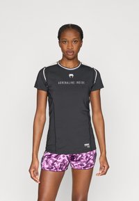 Μαύρο αθλητικό πουκάμισο με κοντά μανίκια, κείμενο «ADRENALINE INSIDE», με αντίθετο τελείωμα· σετ με ροζ σορτς καμουφλάζ. Ομαλό ύφασμα, εφαρμοστό σχέδιο.