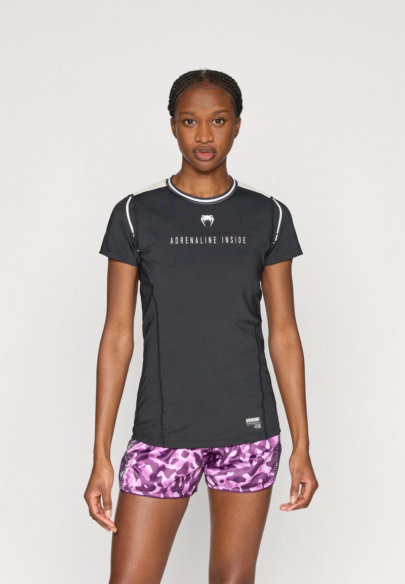 Μαύρο αθλητικό πουκάμισο με κοντά μανίκια, κείμενο «ADRENALINE INSIDE», με αντίθετο τελείωμα· σετ με ροζ σορτς καμουφλάζ. Ομαλό ύφασμα, εφαρμοστό σχέδιο.