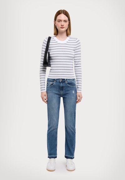 Top cu mâneci lungi în dungi, alb și gri, combinat cu blugi denim de culoare albastru deschis. Încălțămintea este formată din adidași albi, iar accesoriul este o geantă neagră.