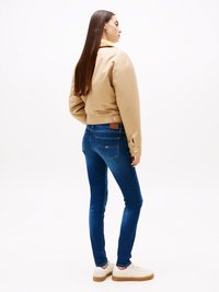 Beige cropped jack met een puntige kraag, blauwe skinny jeans en witte sneakers met een lichtbruine zool. Gladde textuur en een aansluitend ontwerp.