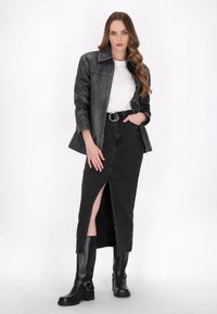 Jachetă de piele neagră, tricou alb, fustă din denim negru cu fante în față și cizme negre până la genunchi cu accente de cataramă. Texturi netede.