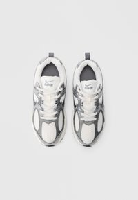 Λευκό και γκρι αθλητικό  παπούτσι με πλέγμα σε επιφάνειες, επένδυση στο κολάρο και κορδόνια· διαθέτει το λογότυπο της Nike και αντανακλαστικές λεπτομέρειες στο πάνω μέρος.