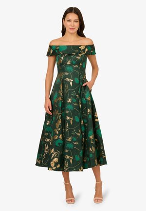 Robe à fleurs vertes avec des accents dorés, forme A-line, tissu texturé, longueur genoux, poches latérales et escarpins assortis.