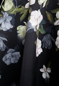 Bloemstoffen met grote witte, roze en blauwe bloemen op een zwarte achtergrond; zachte textuur met gedetailleerde bladeren en natuurlijke patronen.
