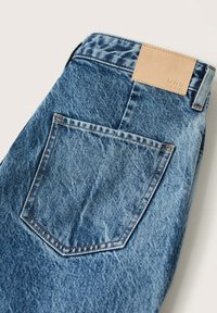 Jeans de mezclilla en azul medio, con un bolsillo trasero rectangular, costuras claras y una etiqueta de cuero marrón claro con la inscripción "MNG DENIM" en la cinturilla.