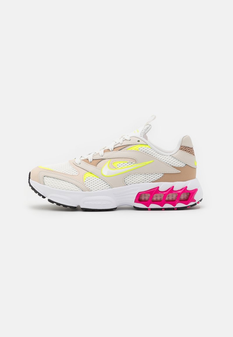 Chaussure de sport blanche et beige avec des accents jaune néon, des panneaux en mesh et un amorti rose visible dans la semelle, vue de côté gauche.