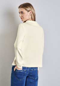 Felpa color crema con maniche lunghe e scollo rotondo, abbinata a jeans in denim blu con tasche posteriori. Design semplice.