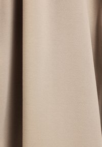 Beige textiel met een gladde oppervlakte, dat een subtiel weefpatroon toont. Het textiel is gedrapeerd, waardoor diepte en zachtheid zichtbaar zijn.