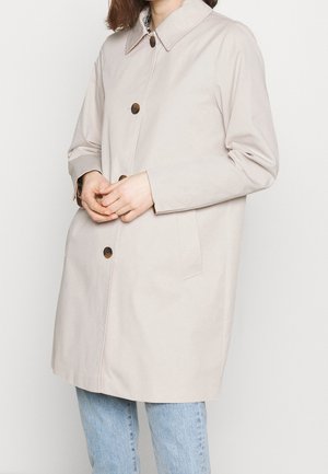 Beige regnrock med krage, framknappar och sidofickor. Tillverkad av ett slätt material med avslappnad passform.