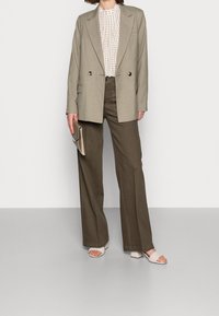 Beige kaksirivinen bleiseri, valkoinen kuviollinen paita, oliivinvihreät leveälahkeiset housut, beige korkopohjainen mules-kenkä, pitää teksturoitua clutch-laukkua.