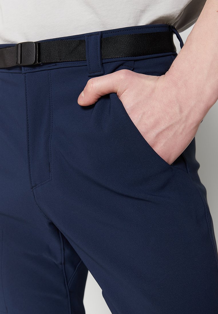 Pantalones azul marino de tejido suave, con un cinturón negro, bolsillos delanteros y un plano cercano de la mano descansando en uno de los bolsillos.