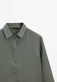 Kravebluse i dæmpet grøn, lavet af tekstureret stof med knaplukning foran og lange ærmer. Simpelt design med klassisk pasform.