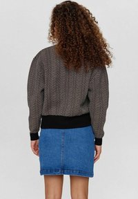 Černobílý svetr s rybí kostí vzorem na pletení, s žebrovaným černým pasem a manžetami, v kombinaci s modrou džínovou minisukní.