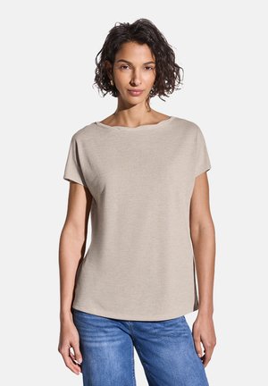 Beige short-sleeve top with a wide neckline, smooth texture, and side slits, paired with blue jeans. Features a relaxed fit.
