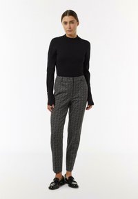 Black fitted sweater with long sleeves, paired with patterned tapered trousers in gray and black, featuring a slim design and glossy black loafers.