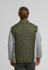 Chaleco acolchado color oliva con un patrón hexagonal, mangas grises en contraste, textura suave y cuello con solapa. Ideal para superponer.