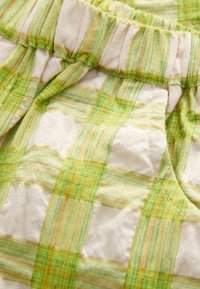 Tissu à carreaux vert et jaune avec une taille froncée et une texture douce, présentant des rayures alternées dans différentes teintes.