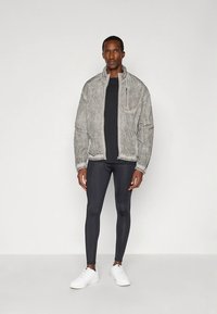 Helehall tekstuuriga bomberjope kõrge kraega, lukuga ja kontrastse musta aluskihtidega. Modell kannab musti retuuse ja valgeid vabaajajalatsid.