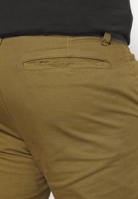 Kaki bukser med en glat tekstur, slim fit og en baglomme med en vandret søm. Taperet design med neutral farve.