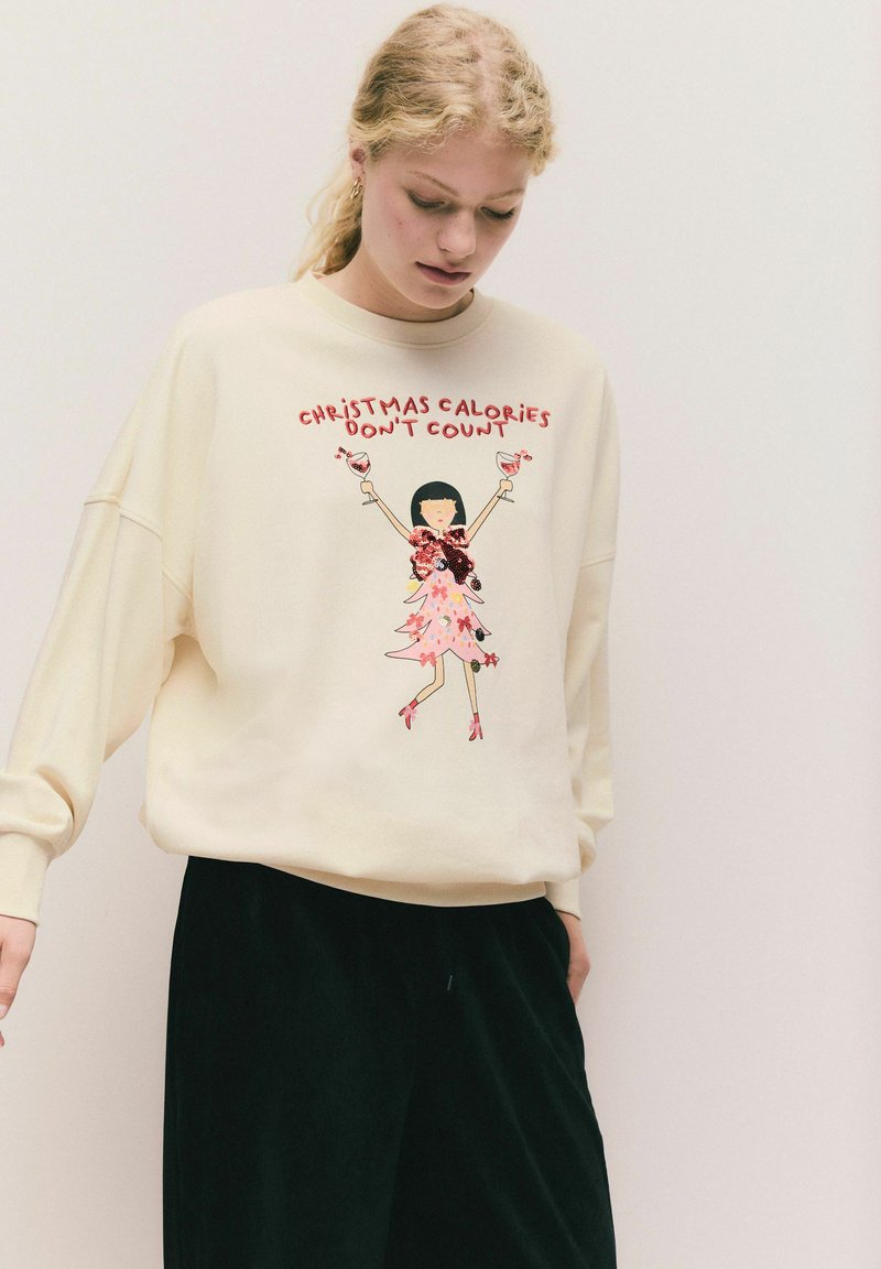 Kermanskat sweatshirt, jossa on rento istuvuus, jossa on graafinen kuva tytöstä, joka pitää pinkkiä dressiä ja cocktaileja sekä teksti: "Joulukalorit eivät vaikuta."